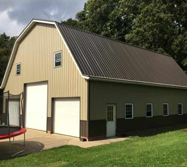 Large gambrel-style barn build with metal roof, vertical siding, and two overhead doors