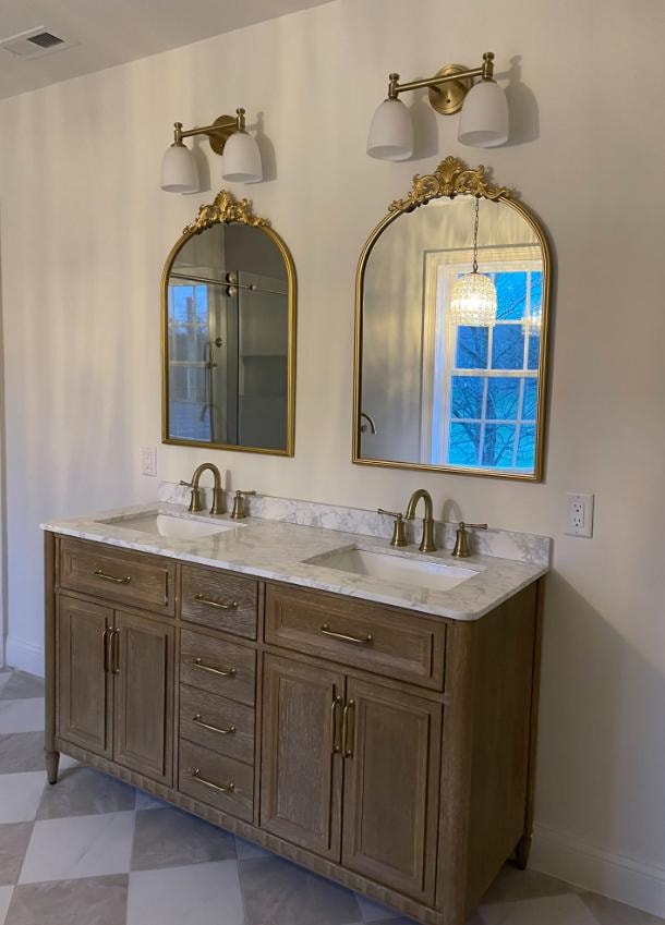 Bathroom remodel with double vanity, marble countertop, ornate gold arch mirrors, and brass sconces