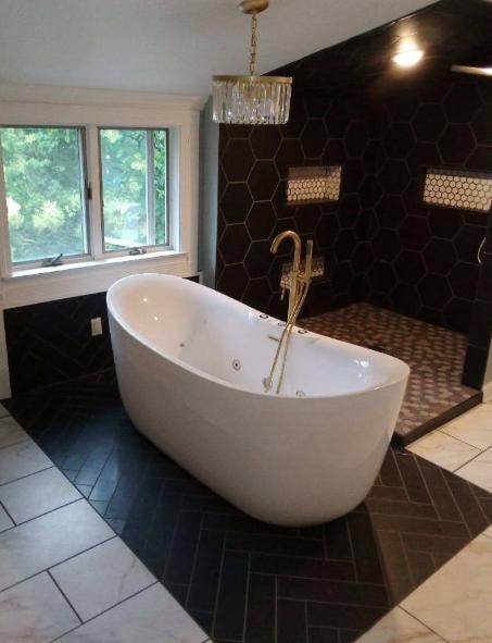Luxury bathroom with freestanding soaking tub, black hexagon tile accent wall, and gold fixtures