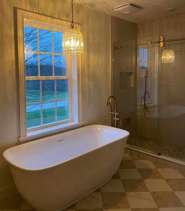 Luxury bathroom with freestanding soaking tub, crystal chandelier, glass shower, and checkered tile