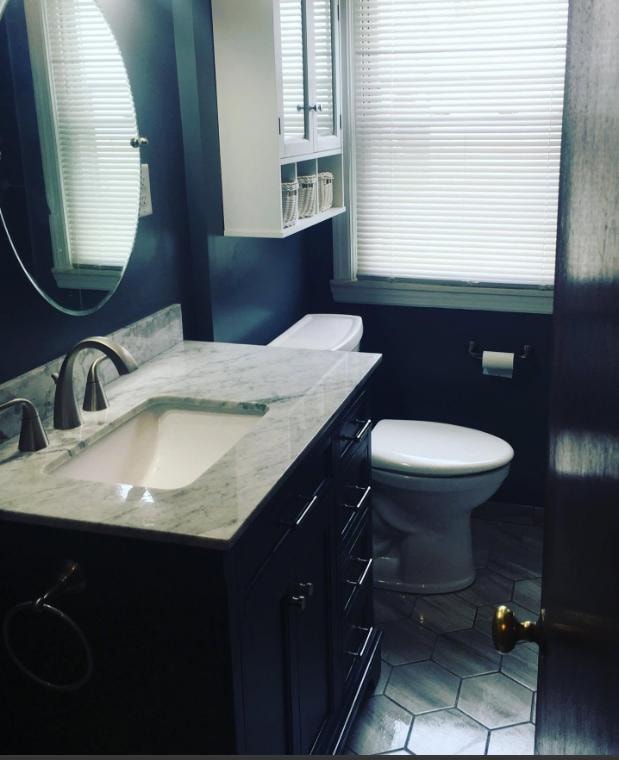Bathroom remodel with navy cabinetry, marble countertop, round mirror, and hex tile floor