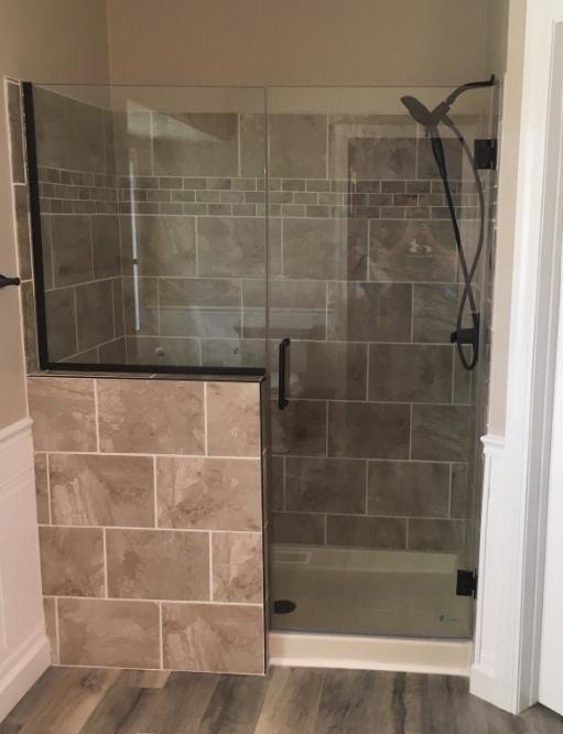 Bathroom shower remodel with beige tile, half-wall entry, frameless glass door, and black fixtures