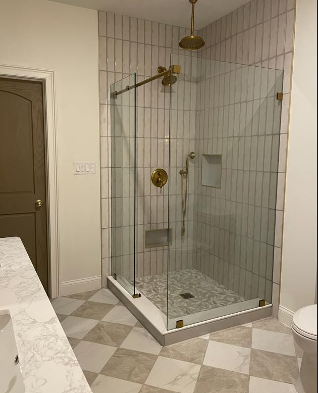 Bathroom remodel with glass shower enclosure, gold fixtures, and marble tile flooring