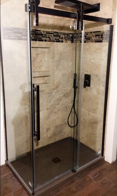 Custom shower with travertine tile, glass mosaic accent band, frameless glass enclosure, and black fixtures