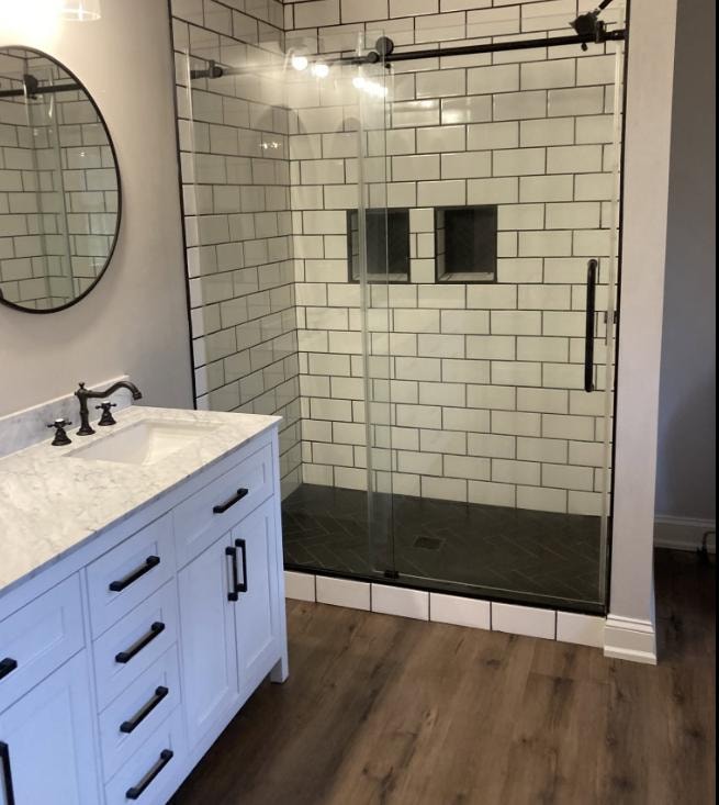 Bathroom renovation with subway tile shower, glass enclosure, white vanity, and black fixtures