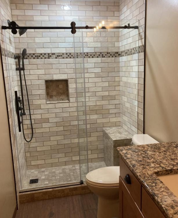 Custom tile shower with decorative mosaic stripe, glass door, and granite countertop