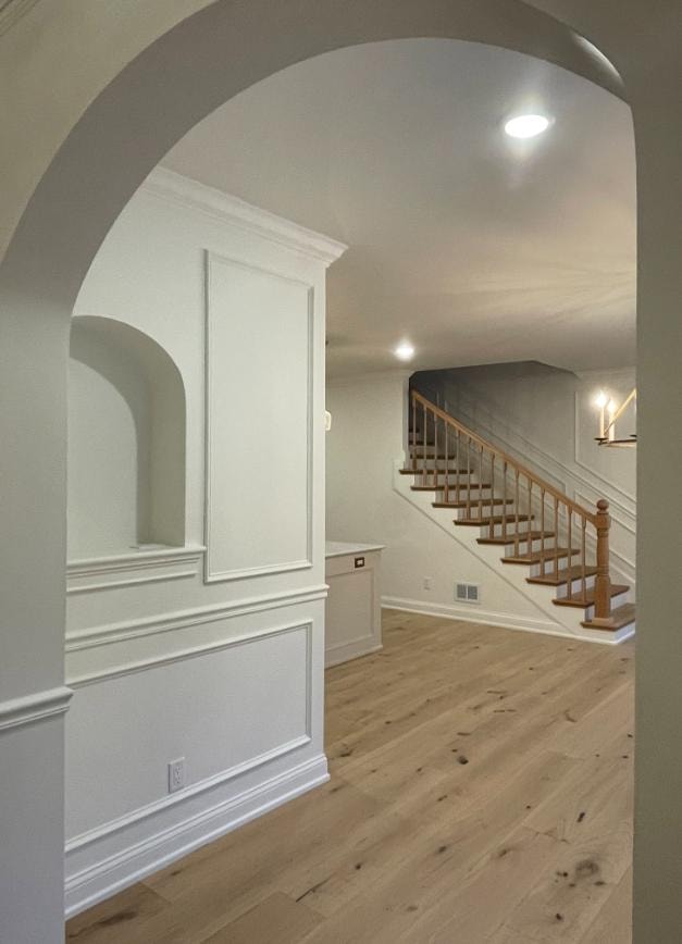 Home addition entryway with arched doorway, wainscoting, wood staircase, and light hardwood floors