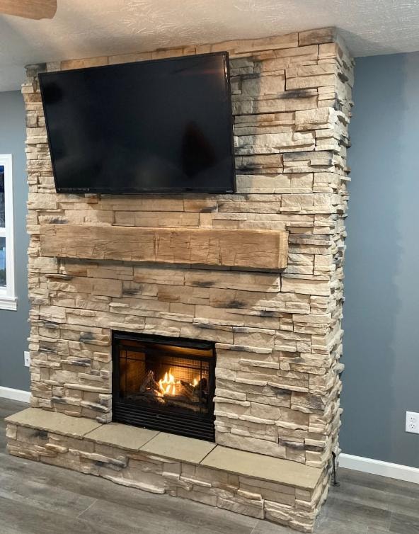 Full stacked stone fireplace with wood beam mantel and mounted TV