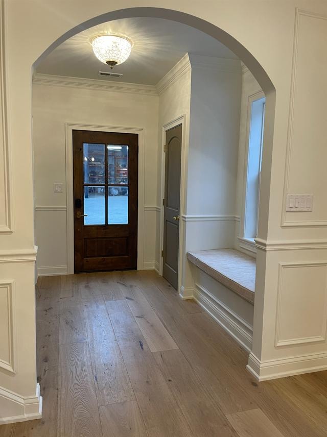 Elegant hallway with arched doorway, crown molding, and hardwood flooring