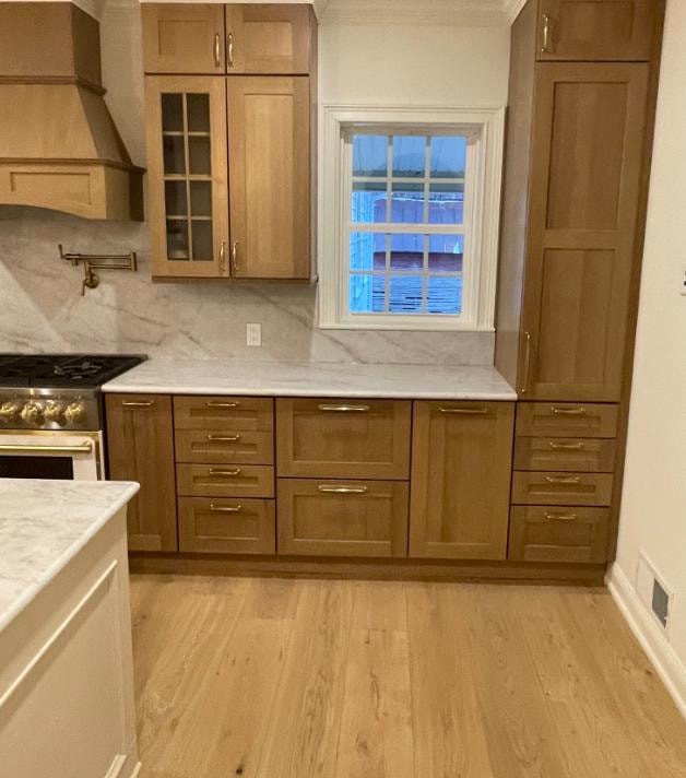 Kitchen remodel detail showing oak cabinetry, marble backsplash, gold range, and hardwood floors