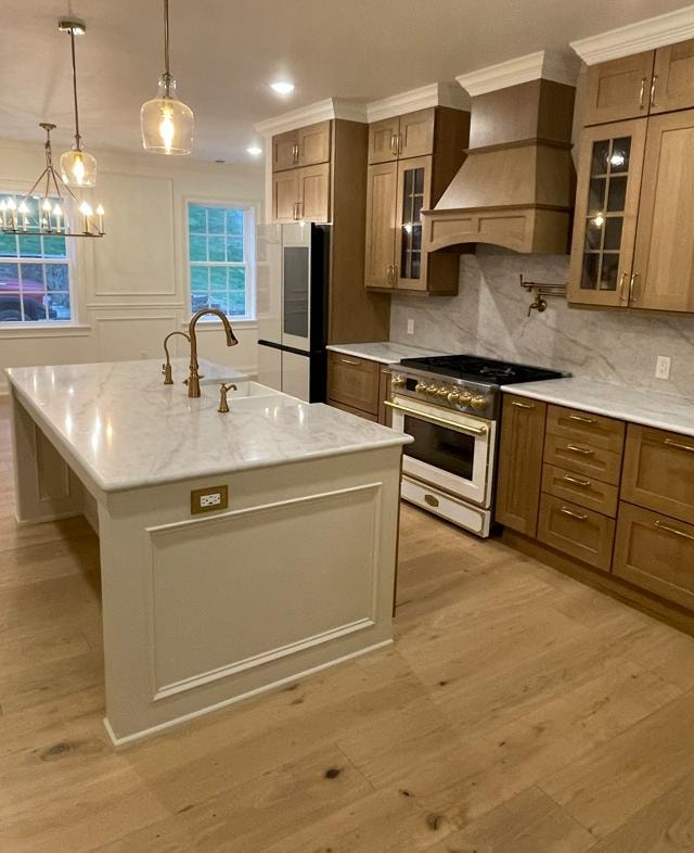 Custom kitchen with wood cabinetry, marble countertops, and gold pendant lighting